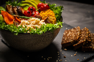 Buddha bowl with vegetables, healthy salad with avocado, carrots, corn and rice, baked chicken breast on a black background. Healthy eating concept. Copyspace. High quality photo