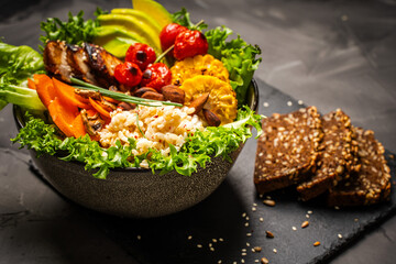 Buddha bowl with vegetables, healthy salad with avocado, carrots, corn and rice, baked chicken breast on a black background. Healthy eating concept. Copyspace. High quality photo