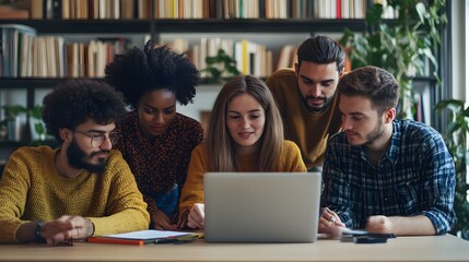 Diverse group of students working together on a laptop in a library.
