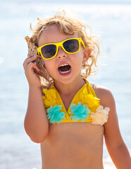 Child listening to a seashell on the sea. Selective focus.