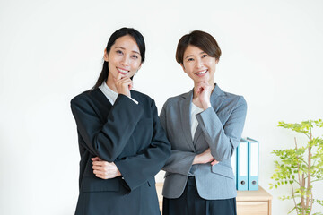白背景で考えるスーツを着た女性二人