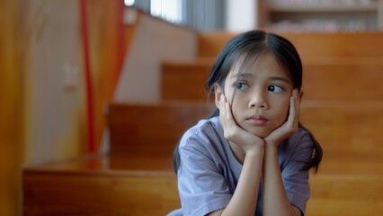 An Asian girl sits on the stairs with a bored expression on her face. Her dim eyes reflect her...