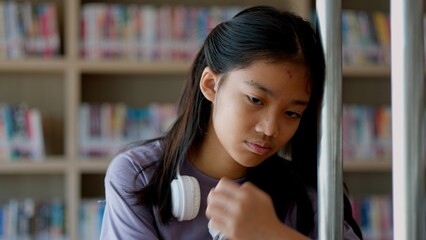 An Asian woman sits on a railing, her face showing stress, boredom, and disappointment.