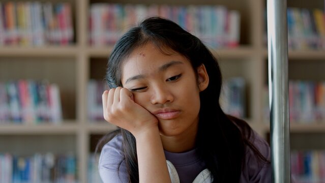 An Asian woman sits on a railing, her face showing stress, boredom, and disappointment. - Powered by Adobe
