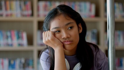 An Asian woman sits on a railing, her face showing stress, boredom, and disappointment.