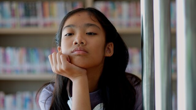An Asian woman sits on a railing, her face showing stress, boredom, and disappointment. - Powered by Adobe