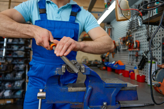 Skilled young handyman correcting metal detail part using bench vise at workshop