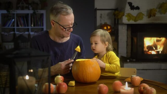 Father and his little son making pumpkin jack o lantern during Halloween celebration at home. Fun craft and decoration at home. Happy toddler boy and his dad preparing for the holiday, decorating the