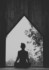 Woman doing Vinyasa yoga pose close to a window with black fitness outfit wooden room natural light black and white
