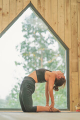 Woman doing vinyasa yoga Camel
Pose beautiful wooden interior