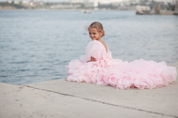 A young lady in a pink princess dress poses on the street, a 7-year-old child model walks along the street of an ancient city. Concept of a postcard