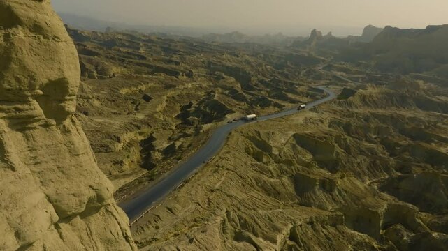 Aerial view of the Makran Coastal Highway in Balochistan, Pakistan, featuring winding roads through dramatic rocky landscapes under a clear sky. push forward shot