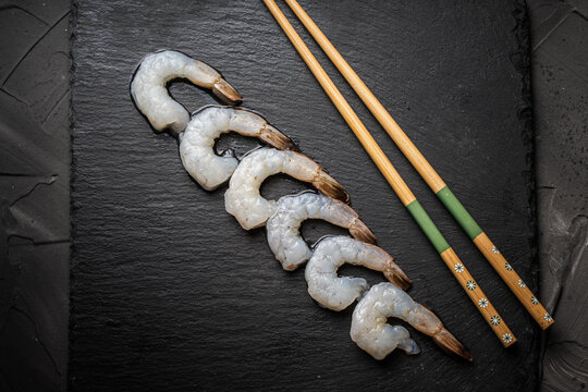 Raw king or tiger prawns arranged in a row with chopsticks on a black mica board, Copy space.