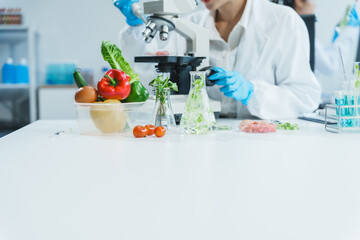 Two Asian women in a lab work on food research, using a microscope, petri dish, and test tubes...