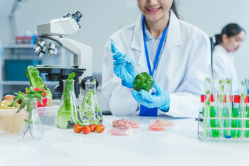 Two Asian women in a lab work on food research, using a microscope, petri dish, and test tubes...