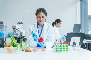 Two Asian women in a lab work on food research, using a microscope, petri dish, and test tubes...