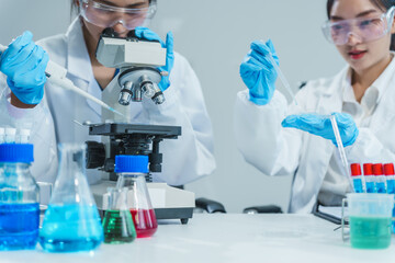 Two Asian women in a lab work on food research, using a microscope, petri dish, and test tubes...