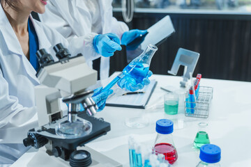 Fototapeta premium Two Asian women in a lab work on food research, using a microscope, petri dish, and test tubes filled with chemical solutions. They study vegetables, pork, and plants for GMO traits and nutrition.
