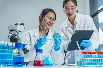 Two Asian women in a lab work on food research, using a microscope, petri dish, and test tubes filled with chemical solutions. They study vegetables, pork, and plants for GMO traits and nutrition.