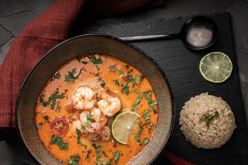 Tom Yam Kung Spicy Thai soup with shrimp in a bowl on a dark background and red pepper, rice and...
