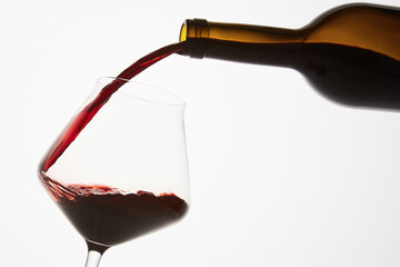 Red wine pouring into tilted wineglass from bottle.