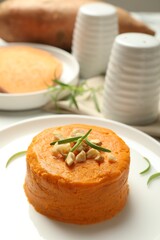 Plate with tasty mashed sweet potato, rosemary and walnuts on table, closeup