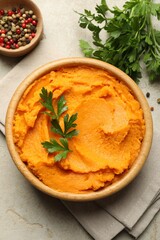 Tasty mashed sweet potato and parsley in bowl on grey textured table, flat lay