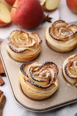Freshly baked apple roses in cupcake pan on table, closeup. Puff pastry
