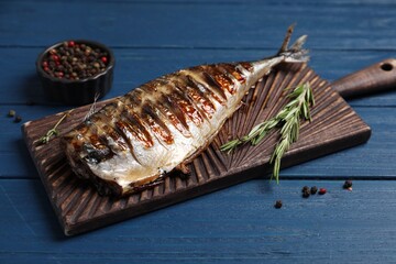 Board with delicious grilled mackerel, peppercorns and rosemary on blue wooden table, closeup