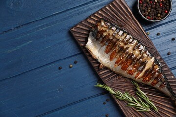 Board with delicious grilled mackerel, peppercorns and rosemary on blue wooden table, flat lay. Space for text