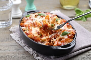 Eating delicious al forno pasta at wooden table, closeup