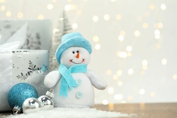 Funny snowman figure and other Christmas decor on artificial snow against blurred lights, space for...