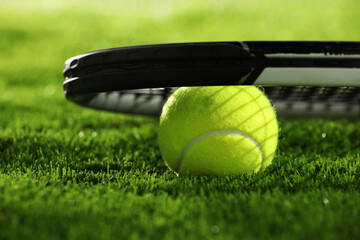 Tennis racket and ball on green grass, closeup