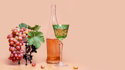  Pink grapes in vase, pink wine in antique crystal glass and bottle on peach background with cut out space for text.