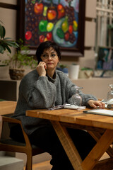 A beautiful brunette woman in a cozy warm sweater is sitting at a table in a restaurant talking on the phone