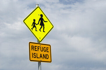 A sign alerts drivers to children crossing the road, while another indicates a refuge island available—a median designed to safeguard pedestrians as they navigate across a multilane road.