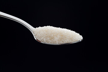 Spoon with sugar crystals on black background