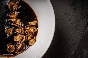 Dried mushrooms are marinated in Thai sauce in a white bowl on a black background.