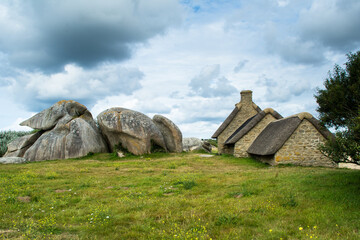 Old stone house with thatched roof and green meadow under cloudy sky in Menehan, Bretagne, France