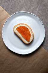Sandwich with butter and red caviar on a white plate.