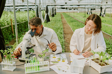 Scientists examining plant samples in modern greenhouse. Scene includes various laboratory...