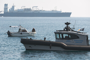 Limassol Coast guard motorboat patrolling with cargo ship in the distance. Akrotiri Bay, Cyprus