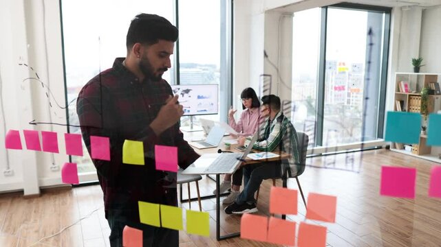 Business team collaborating on project using sticky notes and laptop in modern office. Young professionals discussing ideas and planning strategy during brainstorming session.