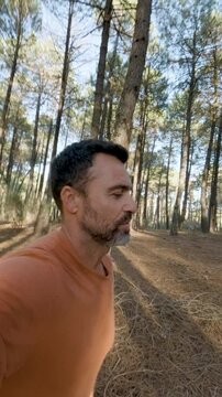 Vertical 4k Slow Motion Video at 25 fps of a Middle-Aged Man Filming Himself Running Through a Mediterranean Pine Forest at Sunset, Turning to Show the Scenic Landscape