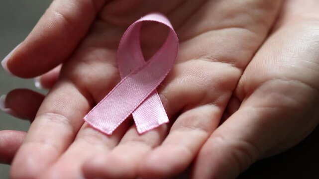 Female hands holding a pink ribbon on open palms, closeup. Breast cancer awareness month and medical oncology prevention concept.
