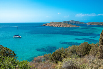 A boat in the Mediterranean Sea near Capo Malfatano, Sardinia, Italy. The setting includes the emerald sea, sky, and a mountainous coastline in the background.
