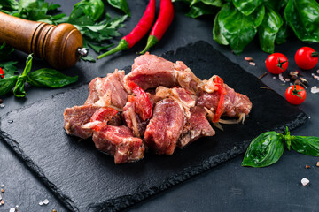 Marinated raw barbecue pork with spices, tomatoes, sweet pepper and onion on a dark background.