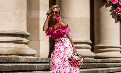 Elegant, stylish woman in pink floral dress and sexy high heels is sensually walking in the city on...