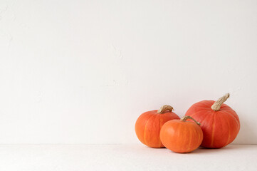 Three pumpkins on neutral light beige table and soft white wall background with empty copy space, autumn holiday backdrop, minimal aesthetic Halloween or Thanksgiving banner design template