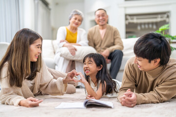 Asian father and mother with daughter bonding time, learning and reading book together on floor, family education at home, nurturing childhood development, happy love asian family indoors, lifestyle
